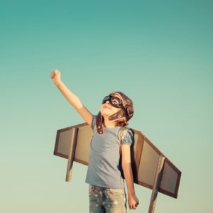 Girl with aviator goggles and wings and arm pointing to sky